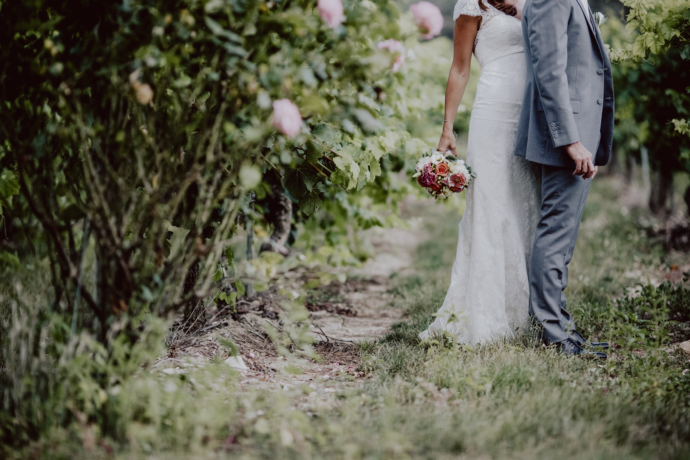 couple de mariés dans une allée de vignes et de roses