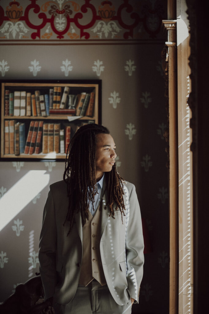 Portrait du marié en costume trois-pièces beige devant une bibliothèque ancienne, lumière naturelle de la Villa Rocabella
